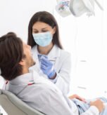 Side view of man having check up in new dental office, assisting by young professional dentist, copy space