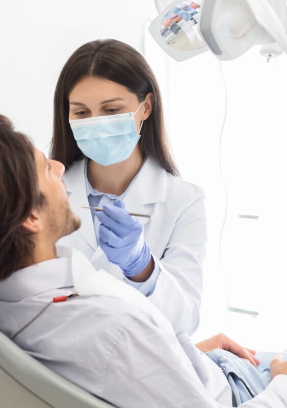 Side view of man having check up in new dental office, assisting by young professional dentist, copy space