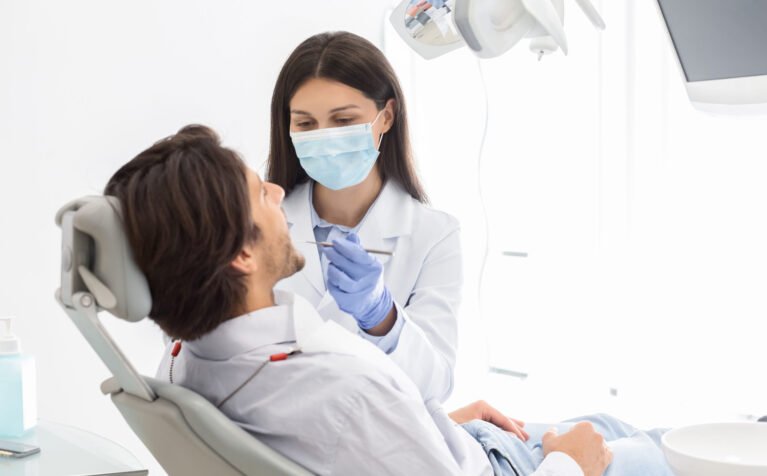 Side view of man having check up in new dental office, assisting by young professional dentist, copy space
