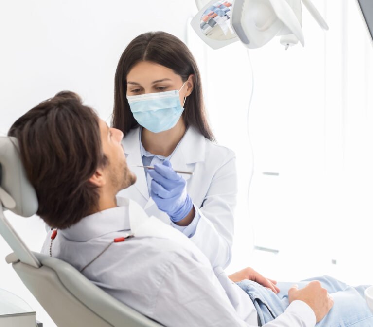 Side view of man having check up in new dental office, assisting by young professional dentist, copy space